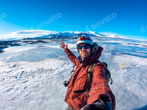 Preview: A man in a red jacket is taking a selfie in front of a snowy mountain