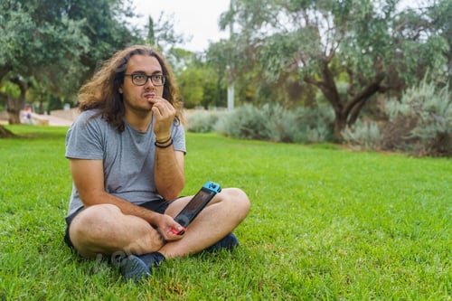 Preview: Man pensive and holding a video game console in the park.
