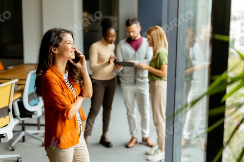 Preview: Young business woman with mobile phone in front of her team at the office