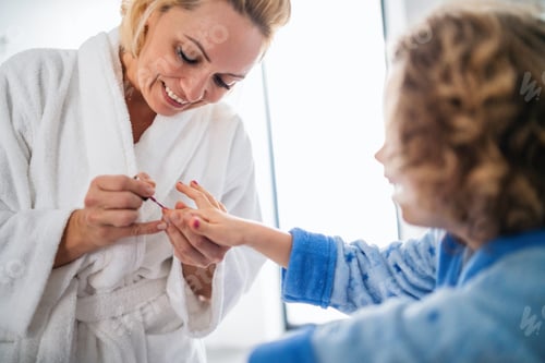 Preview: A cute small girl with mother in bathroom indoors at home, painting nails