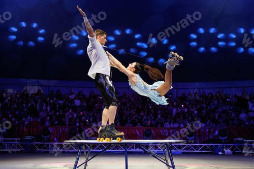 Preview: Young pair of acrobats, man and woman, on roller skates perform in a circus on a small round stage.