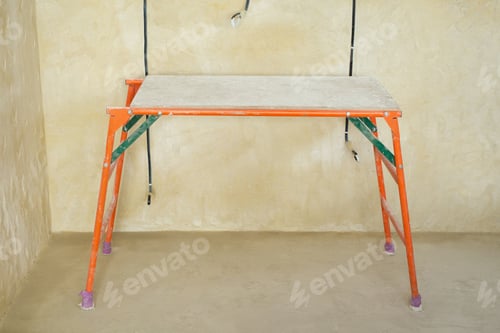 Preview: Iron construction table on the background of the wall. Apartment finishing, plaster and wall putty.