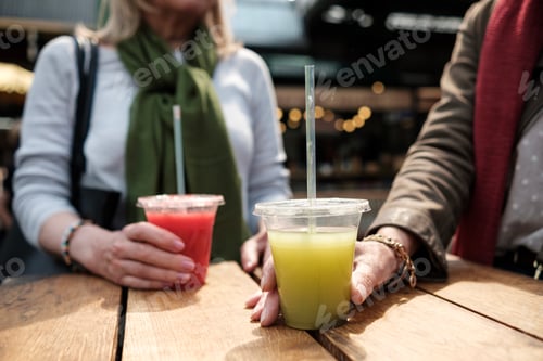 Preview: Close up of two mature women hands holding juice cups on a table.