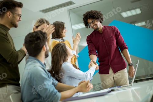 Preview: Group of young coworkers interacting around a table and handshaking in the office