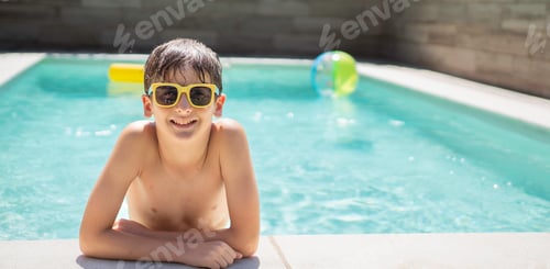 Preview: Front view of smiling boy with sunglasses relaxing at the poolside on a sunny day with copy space.