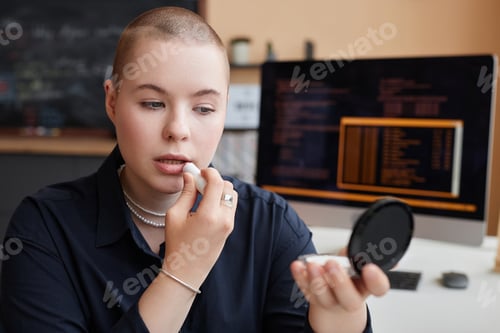 Preview: Bald young businesswoman doing makeup at workplace