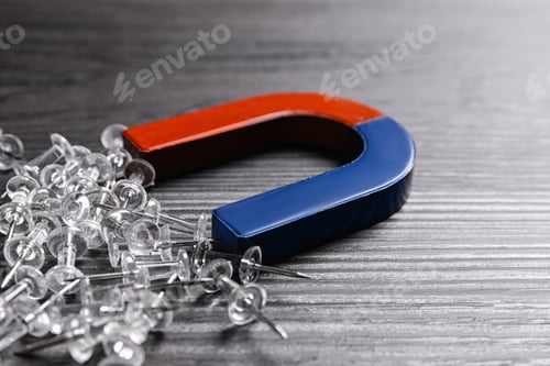 Preview: Magnet attracting drawing pins on dark grey wooden background, closeup
