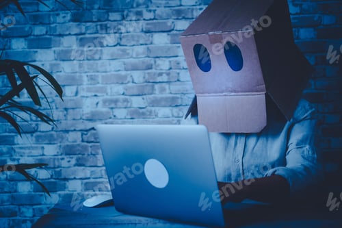 Preview: Anonymous hacker use laptop computer and connection at home wearing a box on his head