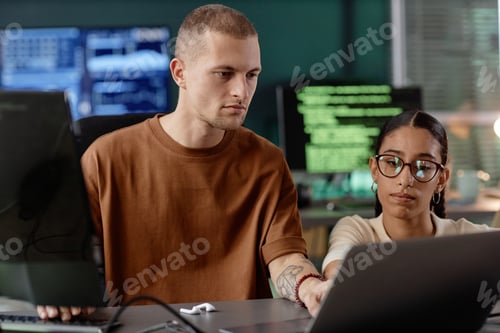 Preview: Focused Male IT Programmer Using Laptop Assisting Colleague at Workplace