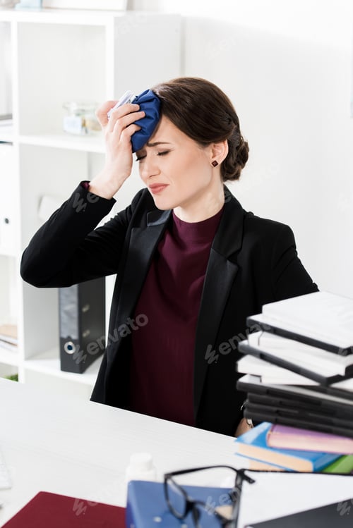 Preview: unhealthy businesswoman touching head with ice pack in office