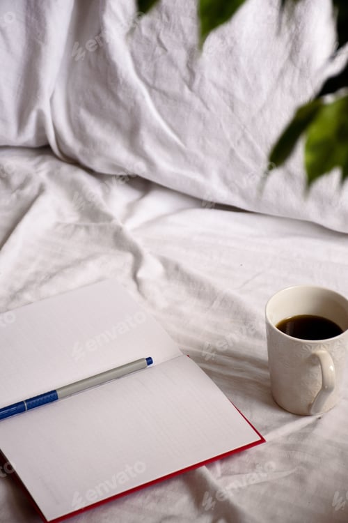Preview: Open notebook with a cup of coffee on a bed with white sheets