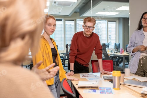 Preview: Confident young intercultural brokers looking and listening to mature colleague