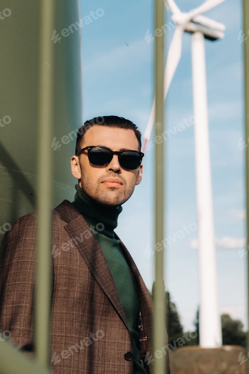Preview: A man in a business suit with a green Golf shirt stands next to a windmill against the background of
