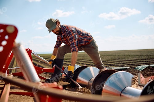 Preview: Farm worker removing soil from disc harrows on tractor in the field.