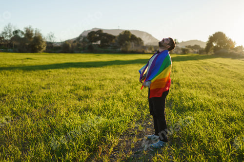 Preview: Man laughing in field at sunset with LGBT flag