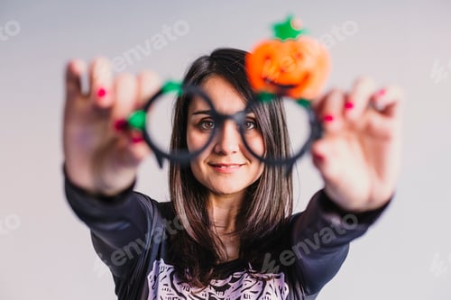 Preview: young woman holding funny halloween glasses and smiling.