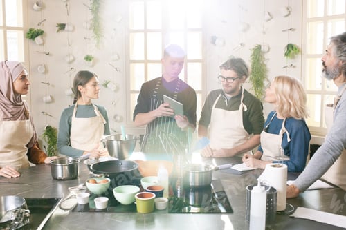 Preview: Group of people in aprons looking at display of tablet held by cooking coach