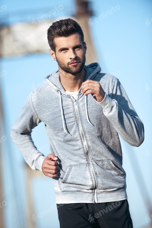 Preview: Keeping his body fit and healthy. Handsome young man looking at camera while running along the road