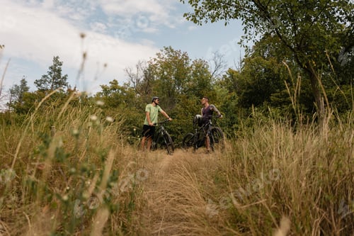 Preview: Two cyclists pause beside their bikes in a scenic grassy forested area