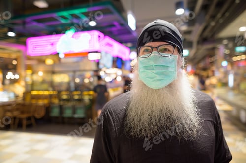 Preview: Mature bearded hipster man thinking with mask for protection from corona virus outbreak at the mall