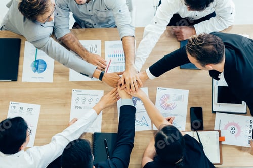Preview: Colleagues stacking hands above table with papers