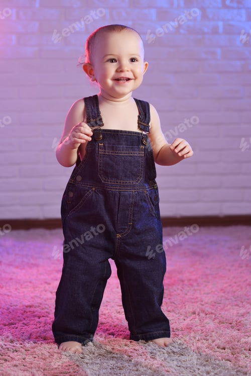 Preview: baby boy in denim overalls smiling while standing barefoot