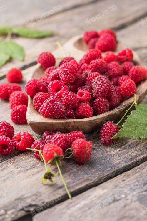 Preview: Appetizing juicy ripe raspberries in a bowl surrounded by green raspberry leaves