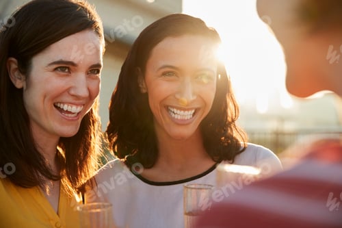 Preview: Female Friends With Drinks Gathered On Rooftop Terrace For Party With City Skyline In Background
