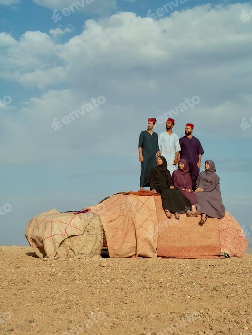 Preview: Group of traditionally dressed individuals posing together on a large rock under a cloudy sky.