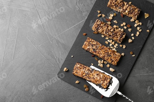 Preview: Slate board with healthy granola bars on grey table, top view. Space for text