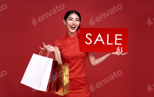 Preview: Happy Asian woman wearing traditional cheongsam qipao dress holding sale sign and shopping bag