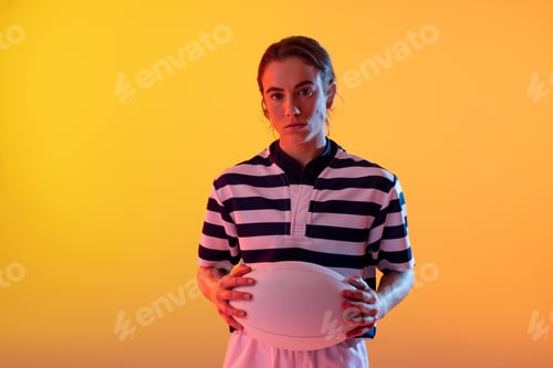 Preview: Portrait of caucasian female rugby player with rugby ball over neon yellow lighting
