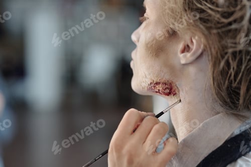 Preview: Hand of stage makeup artist painting wound on face of young man