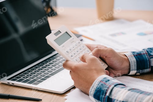 Preview: cropped shot of businessman with calculator working at workplace with documents and laptop