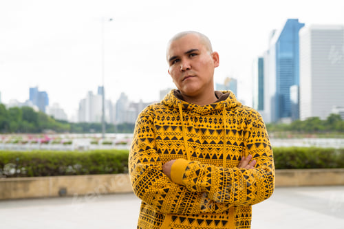 Preview: Young bald Asian man against view of the city at the park