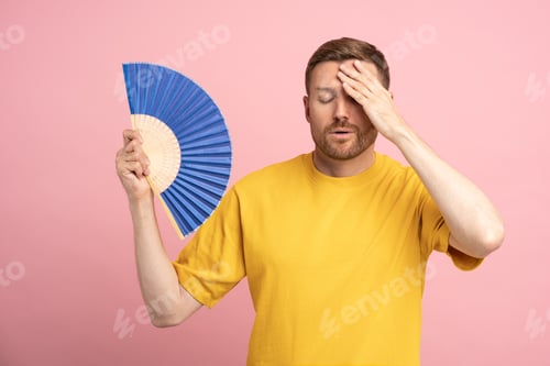 Preview: Sweaty tired man touching forehead using paper fan suffer from heat, cooling in hot summer weather