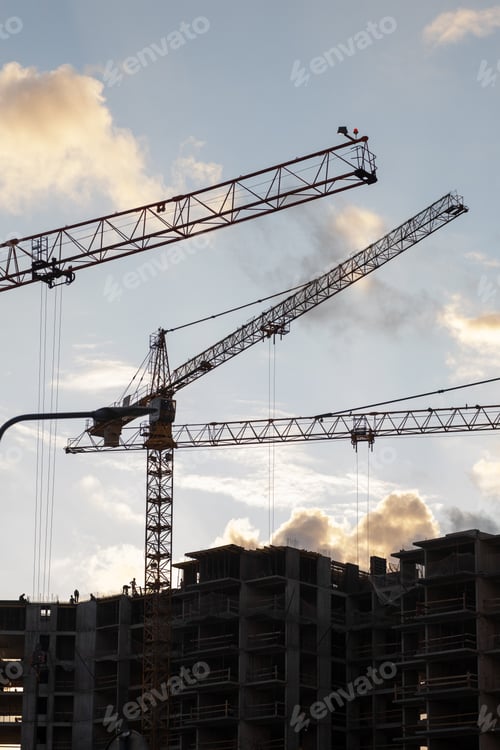 Preview: Several tall cranes are actively lifting materials at a busy construction site as the sun sets