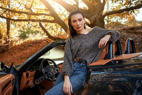 Preview: Sexy young woman in jeans and in a grey sweater sits in a cabriolet