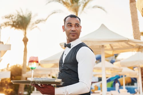Preview: With order in hand. Black waiter in formal clothes is at his work outdoors at sunny daytime
