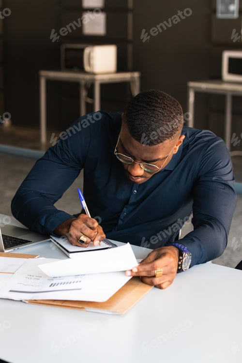 Preview: African American guy writing in notepad near laptop in office