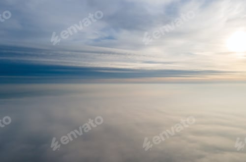 Preview: Aerial view of vibrant yellow sunrise over white dense clouds with blue sky overhead.