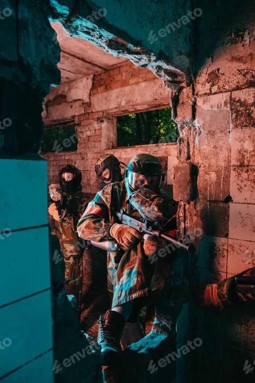 Preview: paintball team in uniform and protective masks playing paintball with marker guns in abandoned