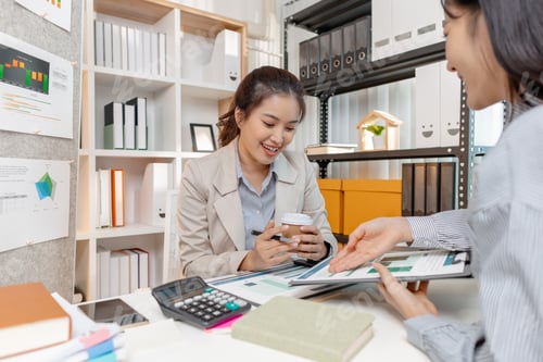 Preview: Two Asian businesswomen discussing ideas and analyzing reports from documents
