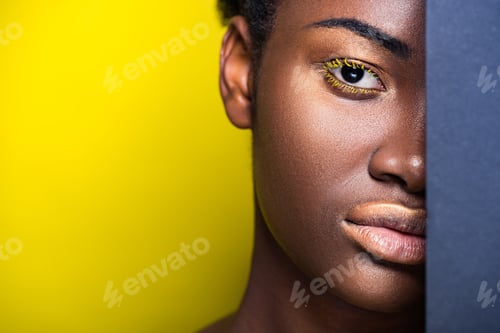 Preview: Cropped view of pretty african american woman with yellow eyelashes looking at camera on yellow
