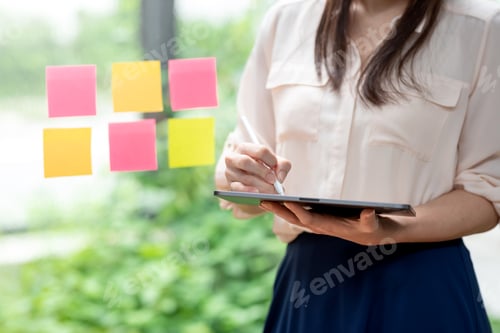 Preview: Close-up of woman holding a stylus working on a tablet standing by the mirror at the office.