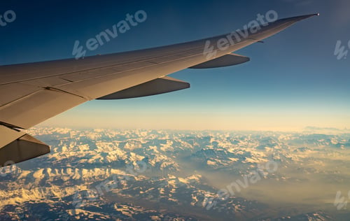 Preview: Wing of plane over mountain cover with white snow. Airplane flying on blue sky. Scenic view from a