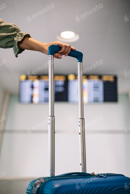 Preview: closeup traveler's hand holding the handle of his luggage in front of the information screens