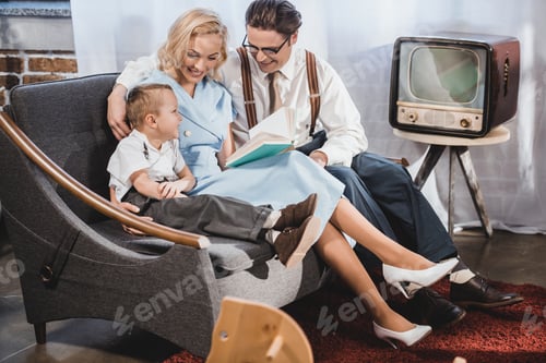 Preview: happy 1950s style family sitting on sofa and reading book together