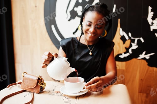 Preview: Young african woman in black blouse at cafe drink tea from teapot.