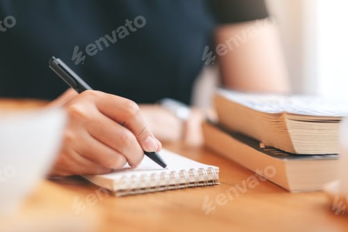 Preview: Closeup image of a woman writing on a blank notebook on wooden table